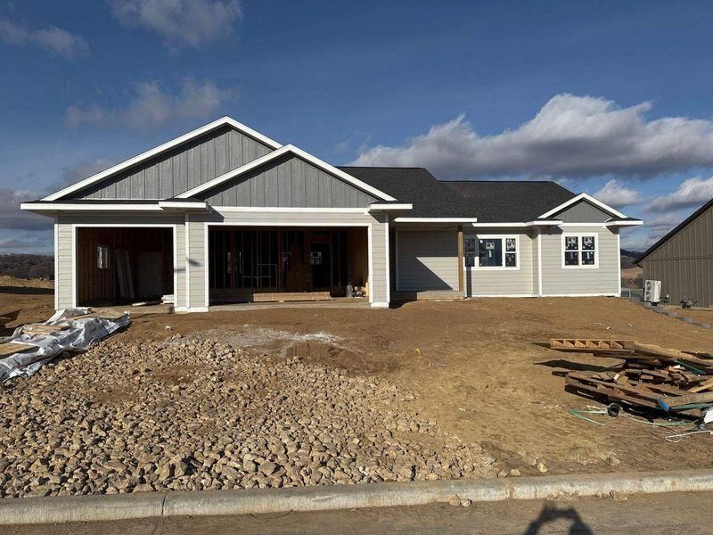 A newly constructed single-story house with gray vertical siding, a white garage, and a dirt yard.