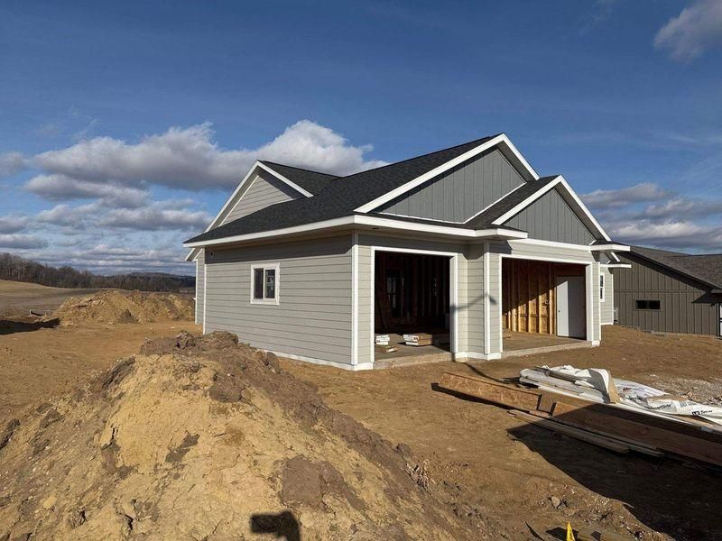 A house under construction with light gray horizontal siding, dark gables, and an open two-car garage.