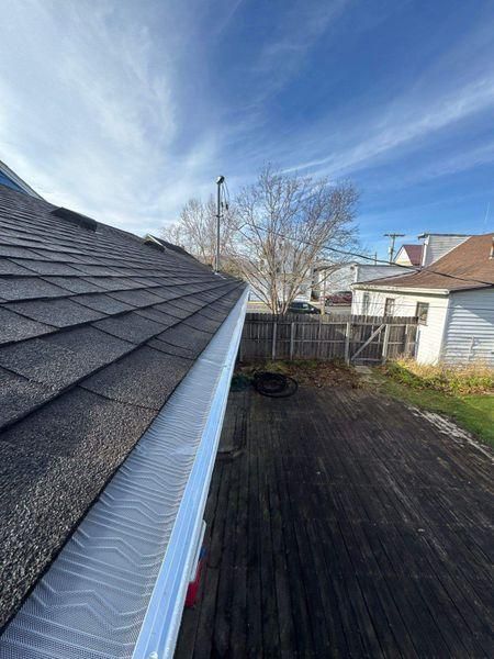 A white gutter with a textured leaf guard attached to a dark shingled roof edge.
