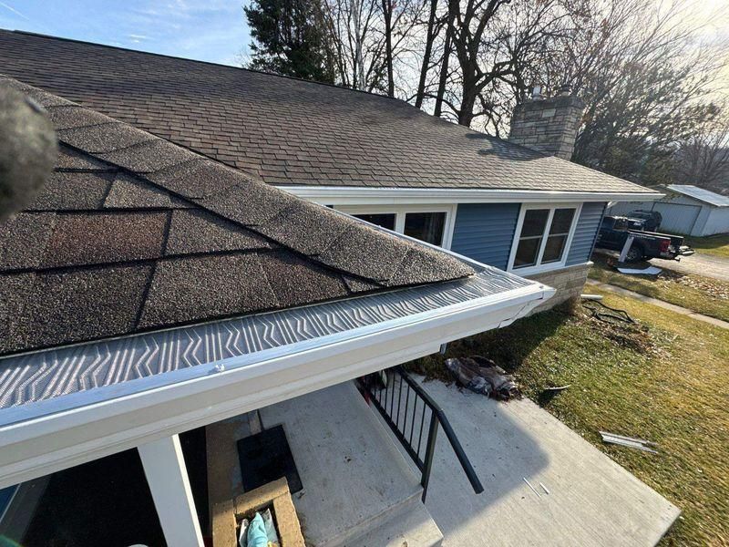 A close-up, high-angle view of a house roof corner with light-colored gutter guards.