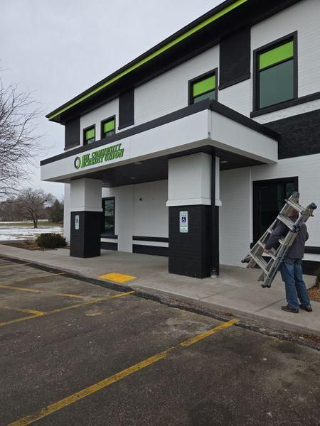 A person carries a ladder toward the entrance of a modern white and black office building.