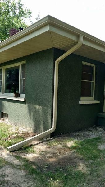 An exterior corner view of a dark green stucco house featuring light-colored gutters.