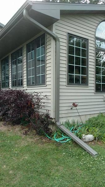 Exterior view of a light-colored house with dark-framed windows, a gutter system, and a landscaping bush.