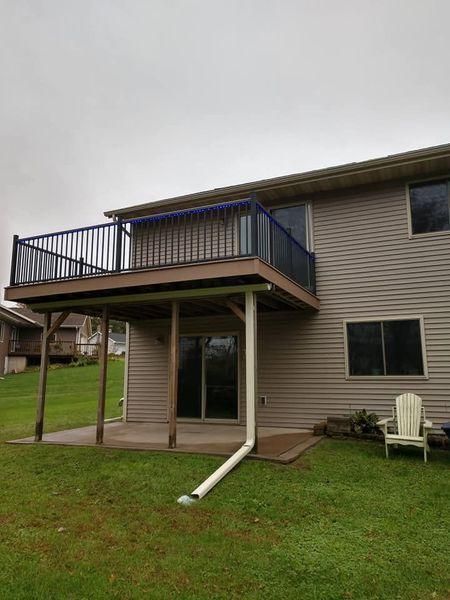An elevated wood deck with black metal railings extends from a light-gray house.