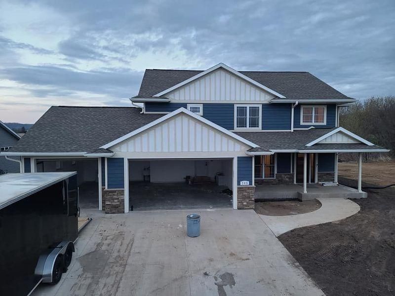 A two-story blue house with white vertical siding, a stone base, and an open garage.