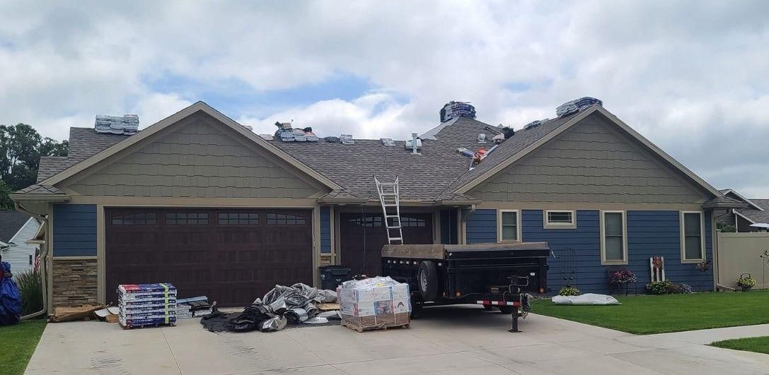 A blue house with a construction trailer and roofing materials in the driveway.