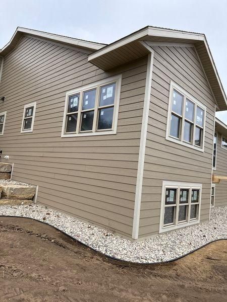 A beige house exterior with white-trimmed windows and a stone and gravel landscape base.