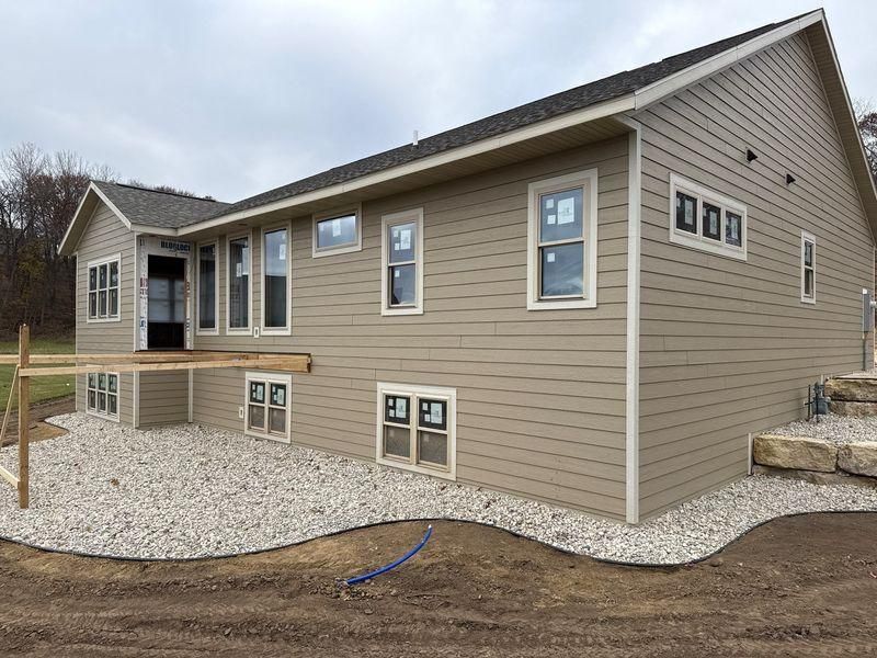 Tan, single-story house with a grey roof, gravel patio, and unfinished wooden deck framing.