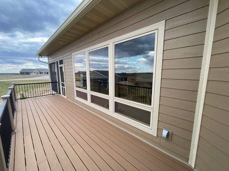A wooden deck with a black railing overlooks an open landscape, adjacent to a house.