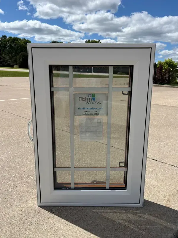 A white vinyl-framed casement window with a decorative grid pattern.