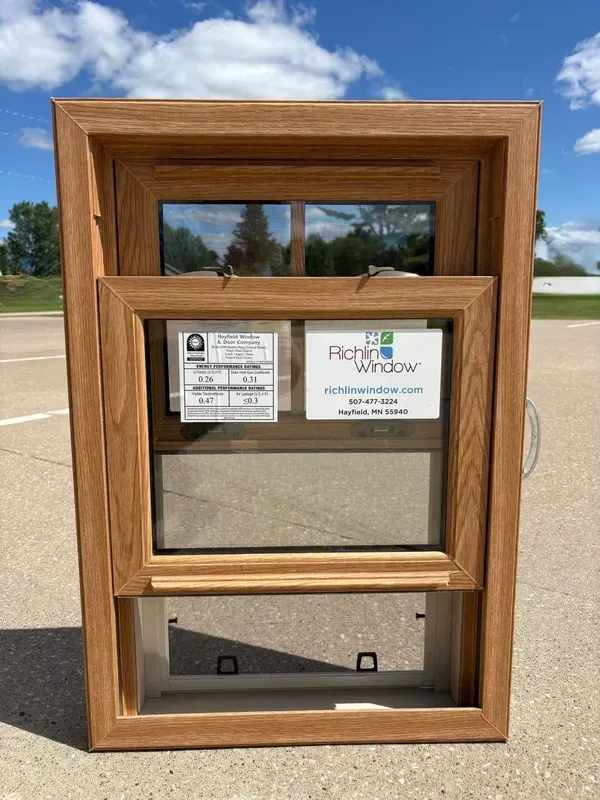 A wood-grain double-hung window sample standing on pavement.