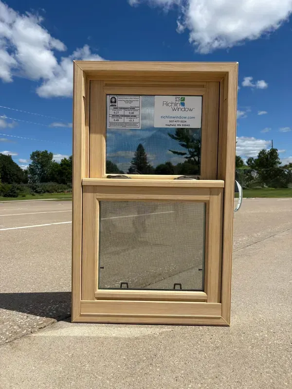 A light-colored wooden single-hung window standing on an outdoor paved surface.