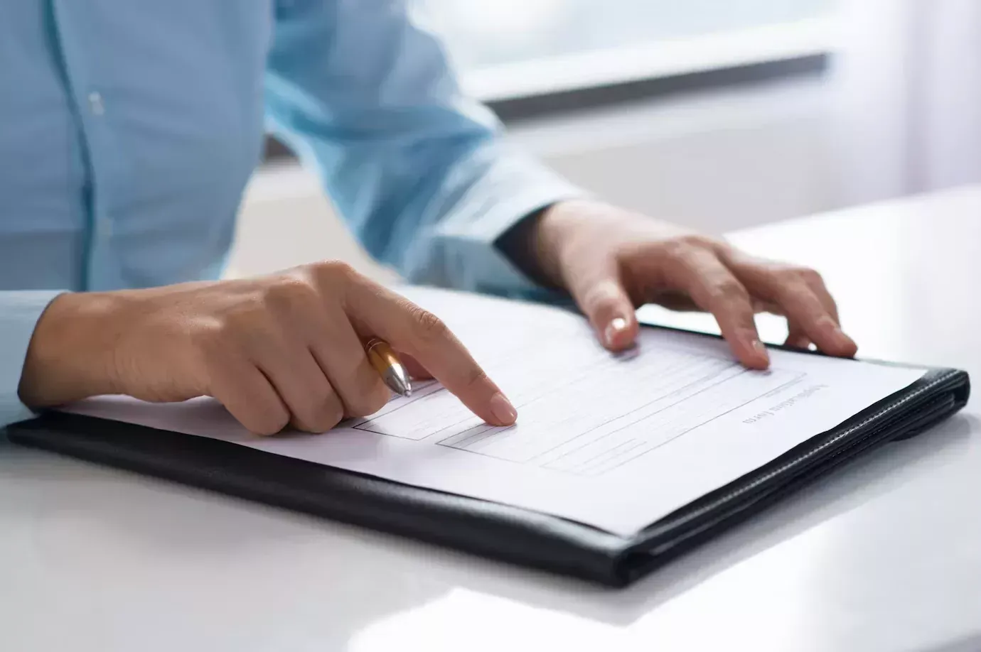 Pessoa vestindo uma camisa azul, sentada, lendo documento.