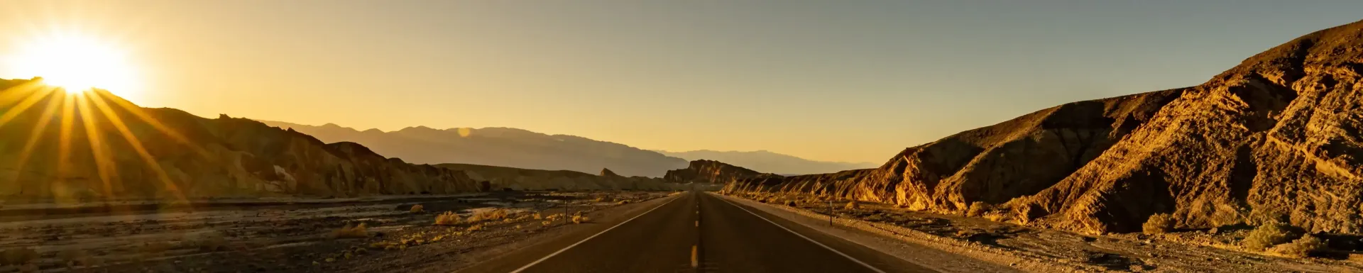 O sol está se pondo sobre uma estrada com montanhas dos dois lados.