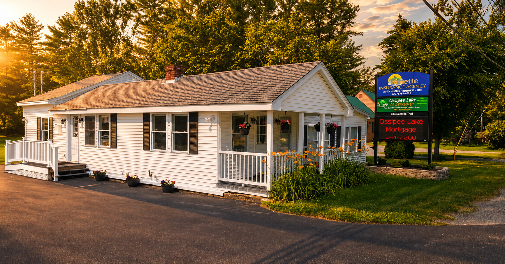 White cottage-style office building at sunset with a roadside sign and surrounding trees.