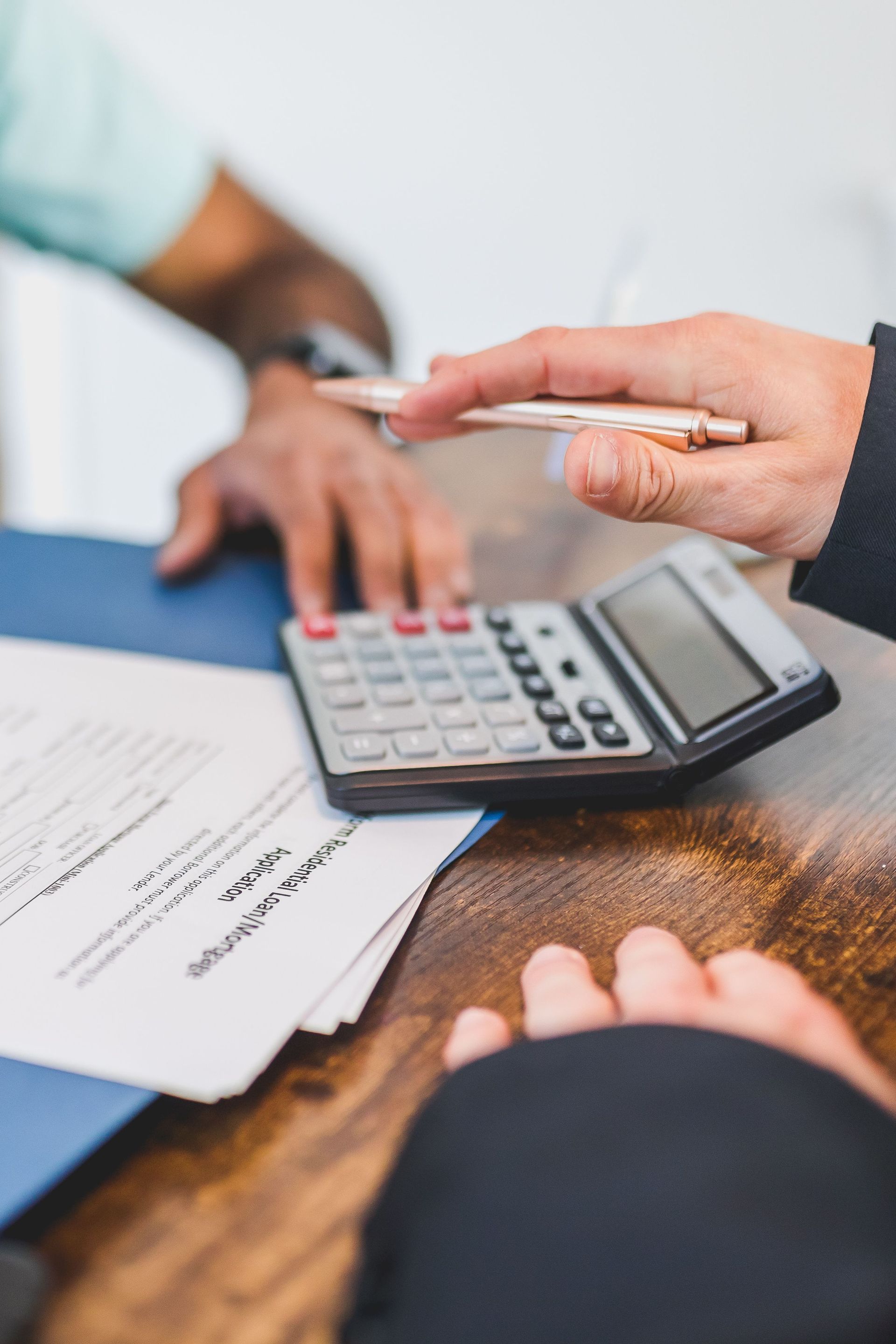 Hands using a calculator over paperwork on a wooden table during a financial discussion