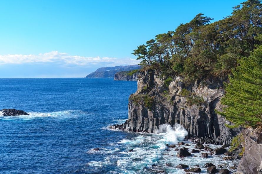 Rocky coastal cliff with waves crashing against dark rock under a clear blue sky