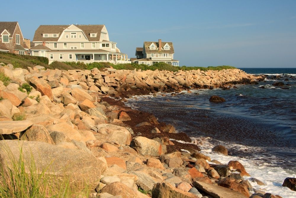 Rocky shoreline with ocean waves and seaside houses under a clear sky