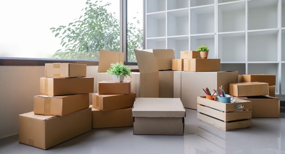 Stacked moving boxes and a couch in a bright, empty room by a window