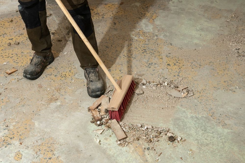 Person sweeping debris from a cracked concrete floor with a broom