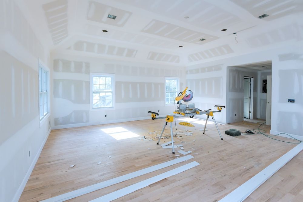 Bright unfinished room with drywall, hardwood floor, and a miter saw on a stand in the center.