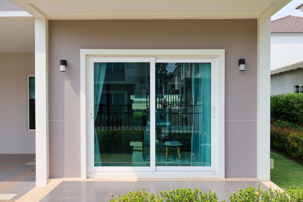 Modern house exterior with a sliding glass door and two wall lights on a beige patio.
