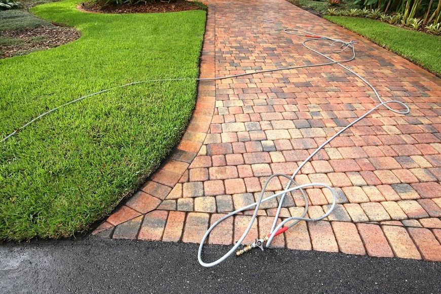 Garden hose on a brick path beside a green lawn.
