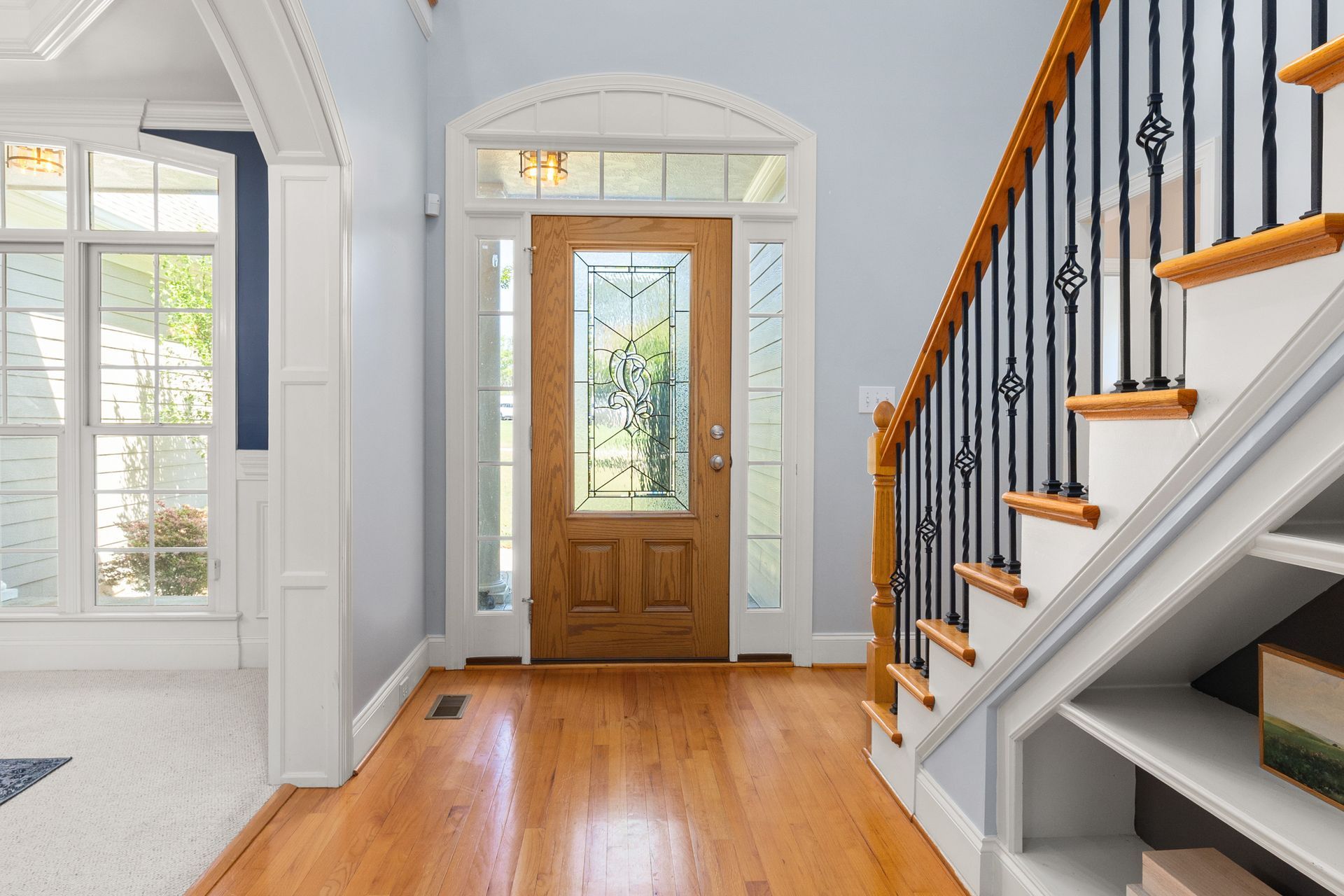 Bright entryway with wood floor, front door, arched openings, and staircase with black railing