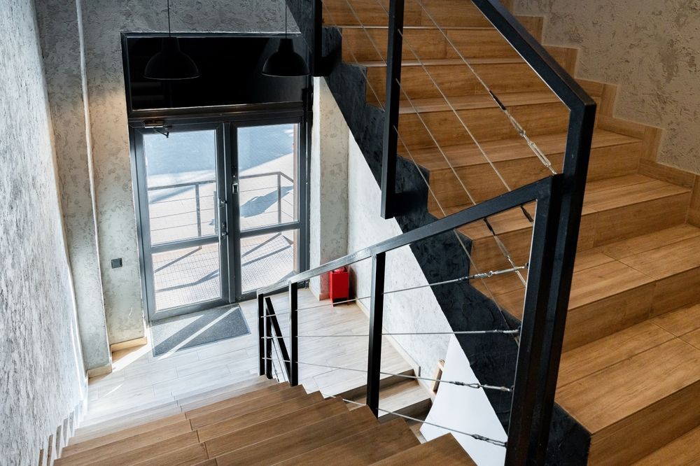 Modern stairwell with wooden steps, black railing, and a glass door at the landing.