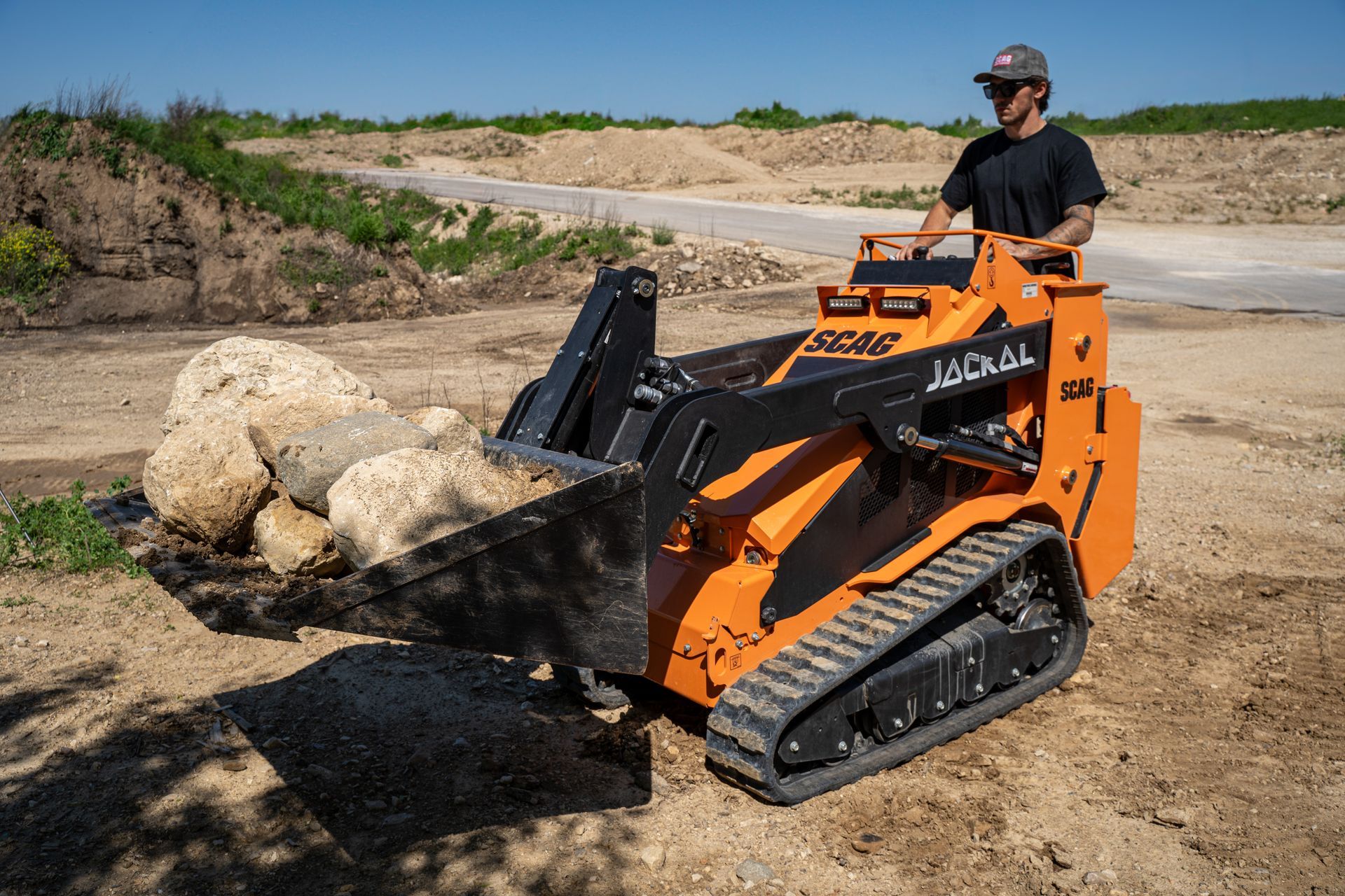 Person operating an orange mini skid steer pushing a large rock on a dirt worksite