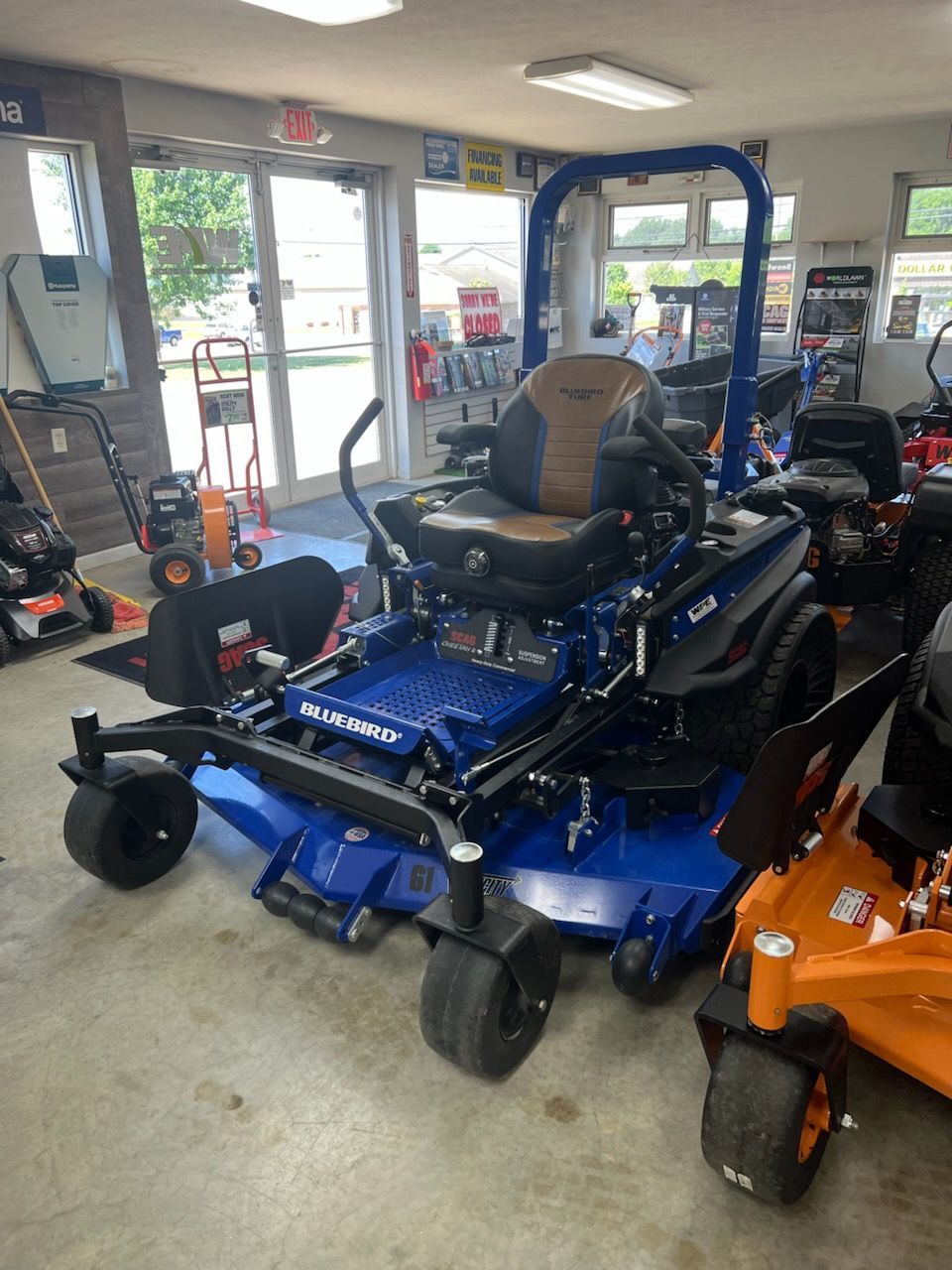 Blue and black zero-turn riding mower with a tan seat, front casters, and wide cutting deck