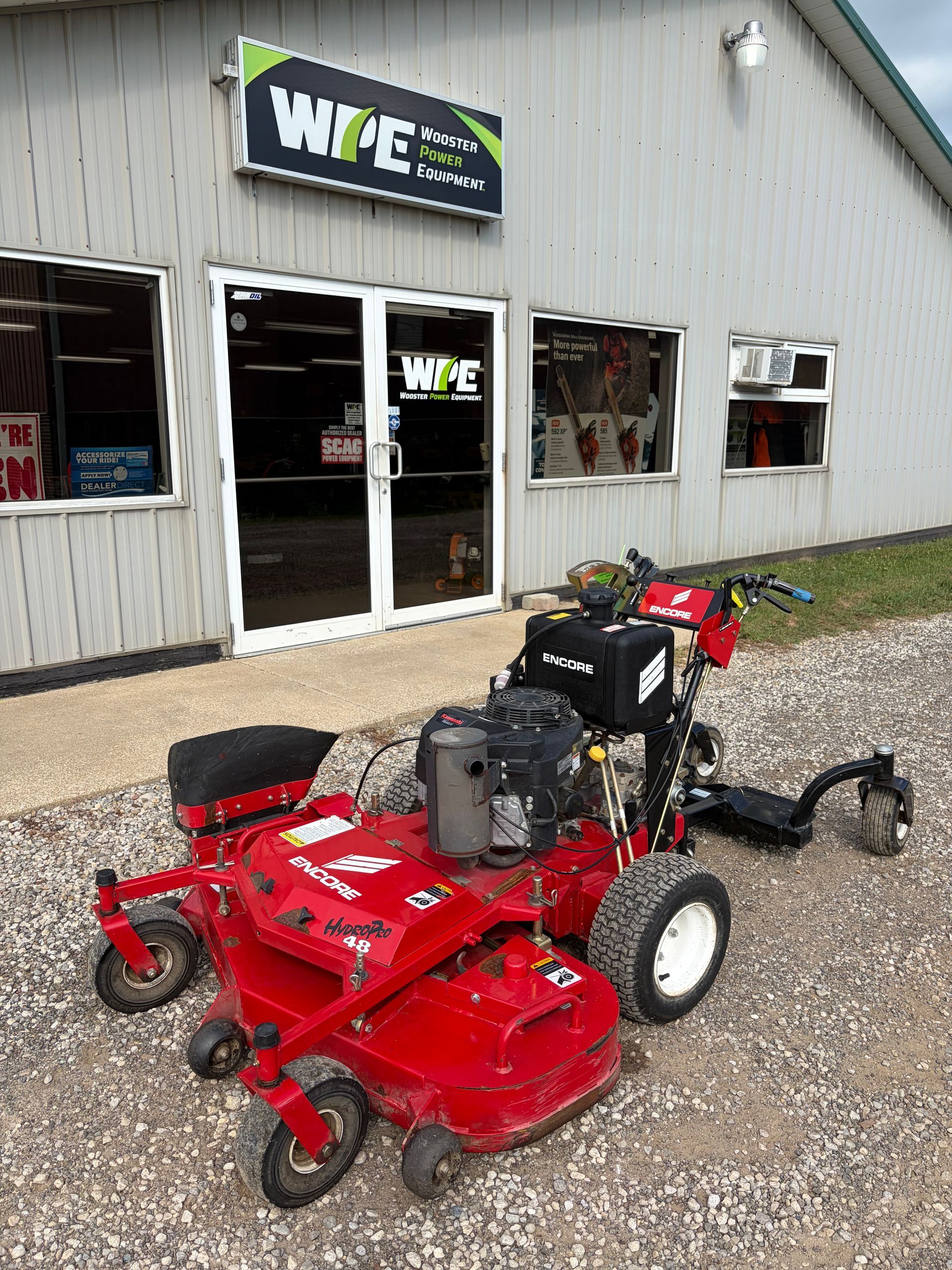 Red riding lawn mower parked outside a beige shop with WFE signs on the building.