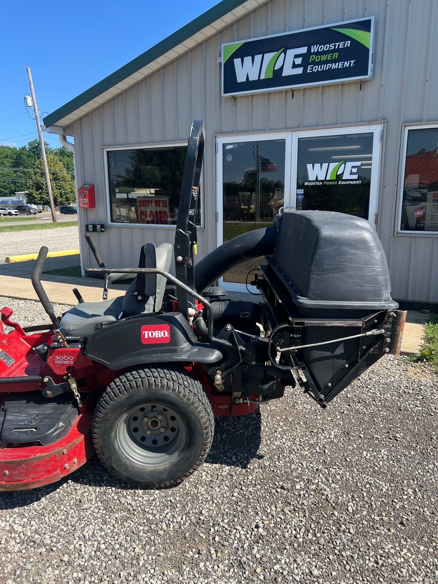 Red riding lawn mower parked outside a beige shop with WFE signs on the building.