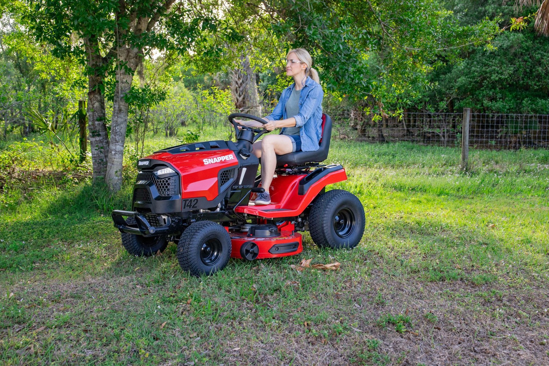 Red Snapper lawn tractor on grass beside a blue house, with a leaf sweeper attachment.