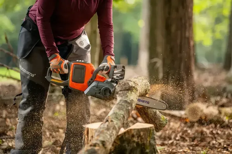 Person using an orange chainsaw to cut a log in a wooded area