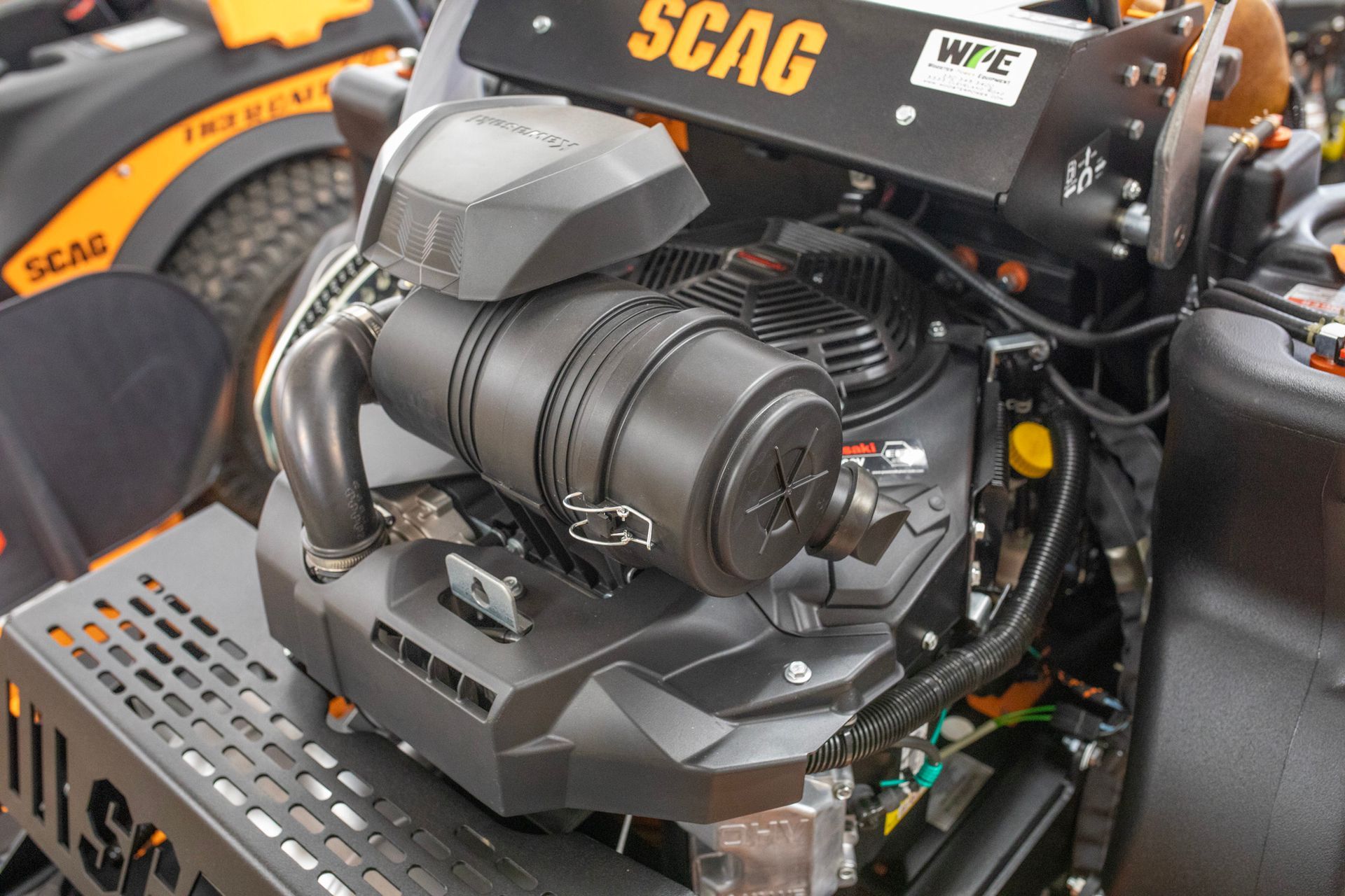Close-up of a SCAG lawn mower engine and battery compartment with black and orange machinery.