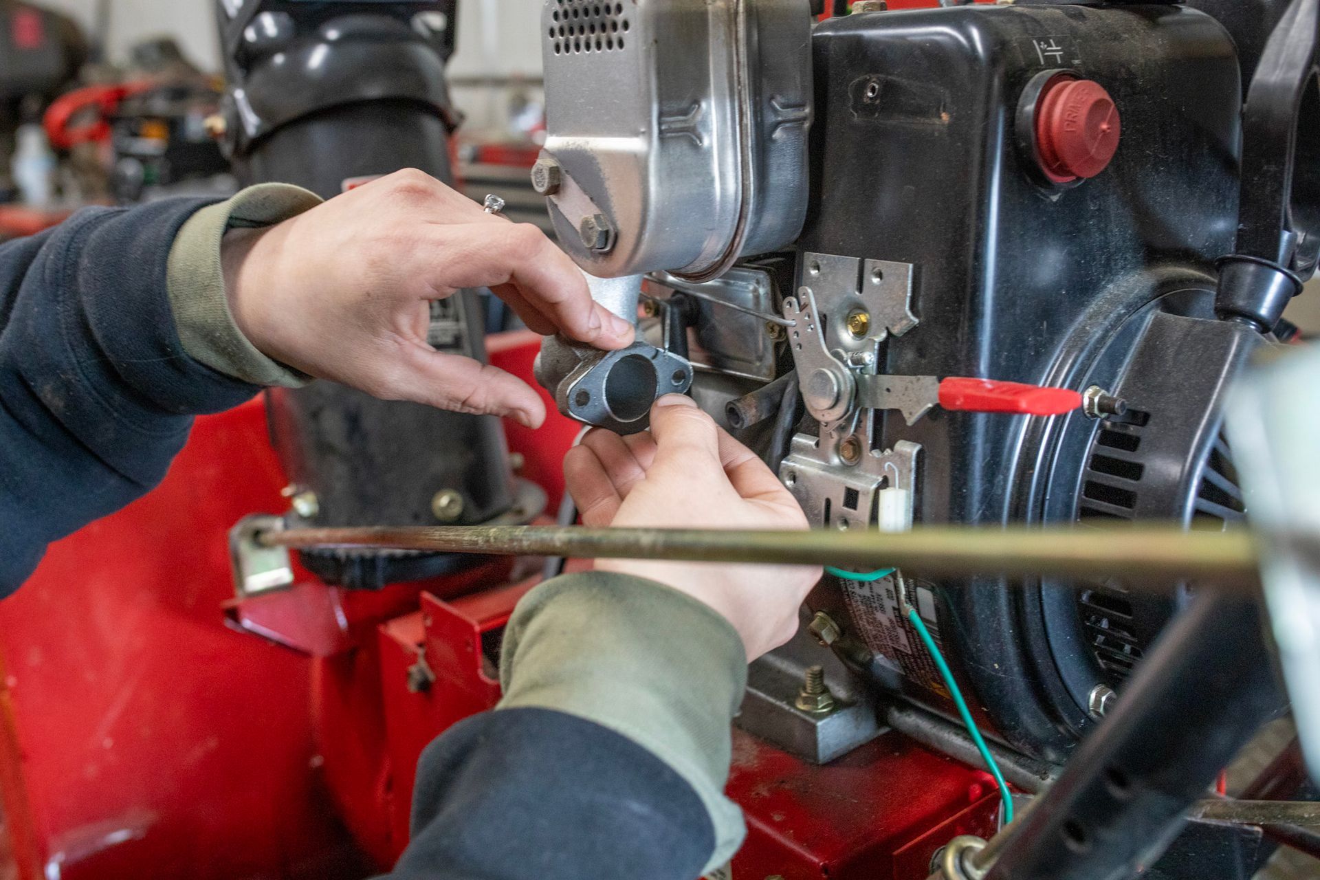 Hands adjusting a machine engine with tools in a red workshop setting