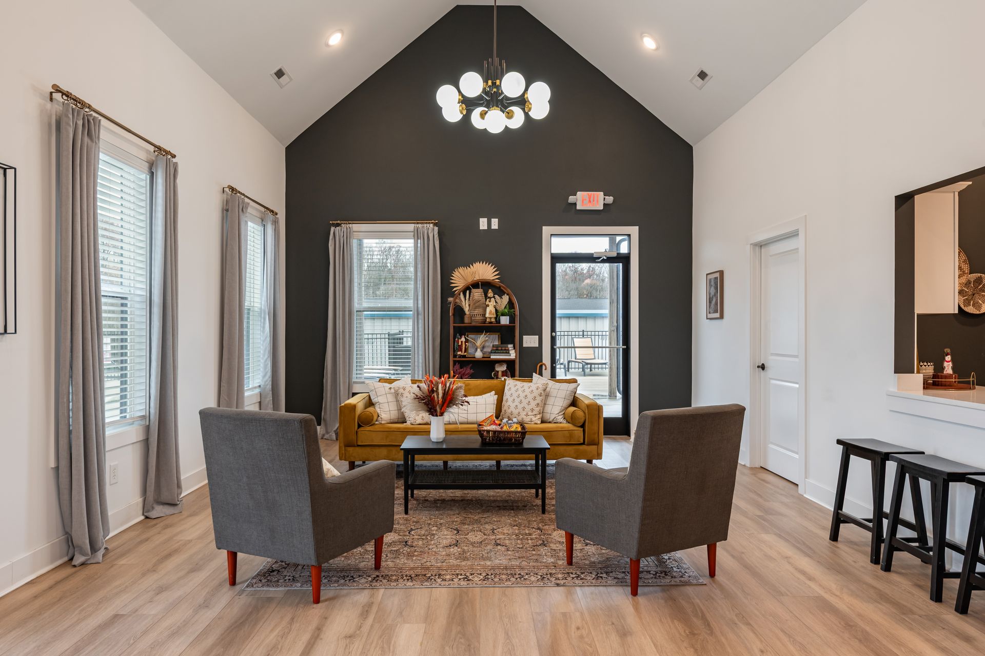 Living room with a mustard-colored sofa, gray armchairs, and a black coffee table in front of a dark gray wall.
