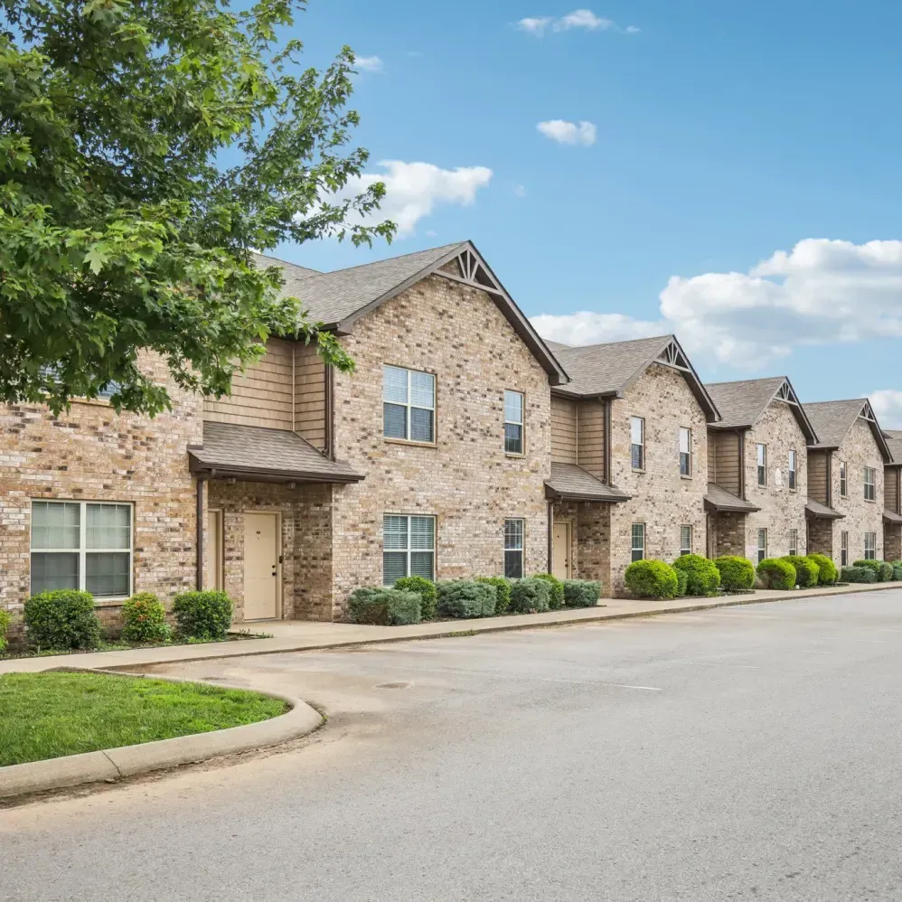 Row of brick townhomes with tan siding, blue sky, and green landscaping.