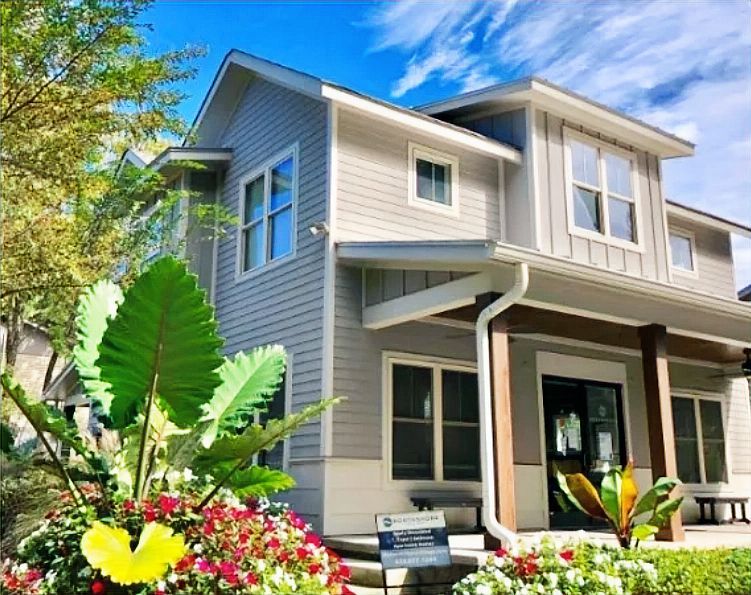 Two-story house with gray siding, white trim, and a porch. Landscaping includes colorful flowers.