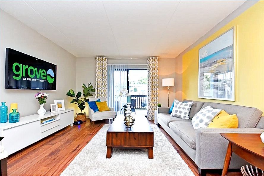 Living room with wood floors, white rug, gray sofa, yellow accent wall, and television.
