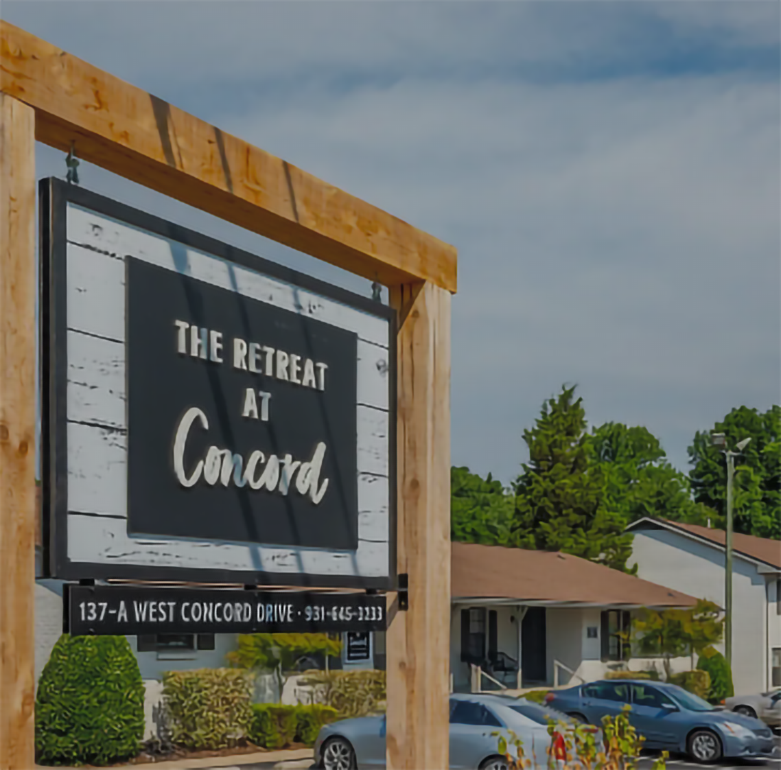Sign for The Retreat at Concord apartments, 137-A West Concord Drive. Blue sky, cars, and buildings in the background.