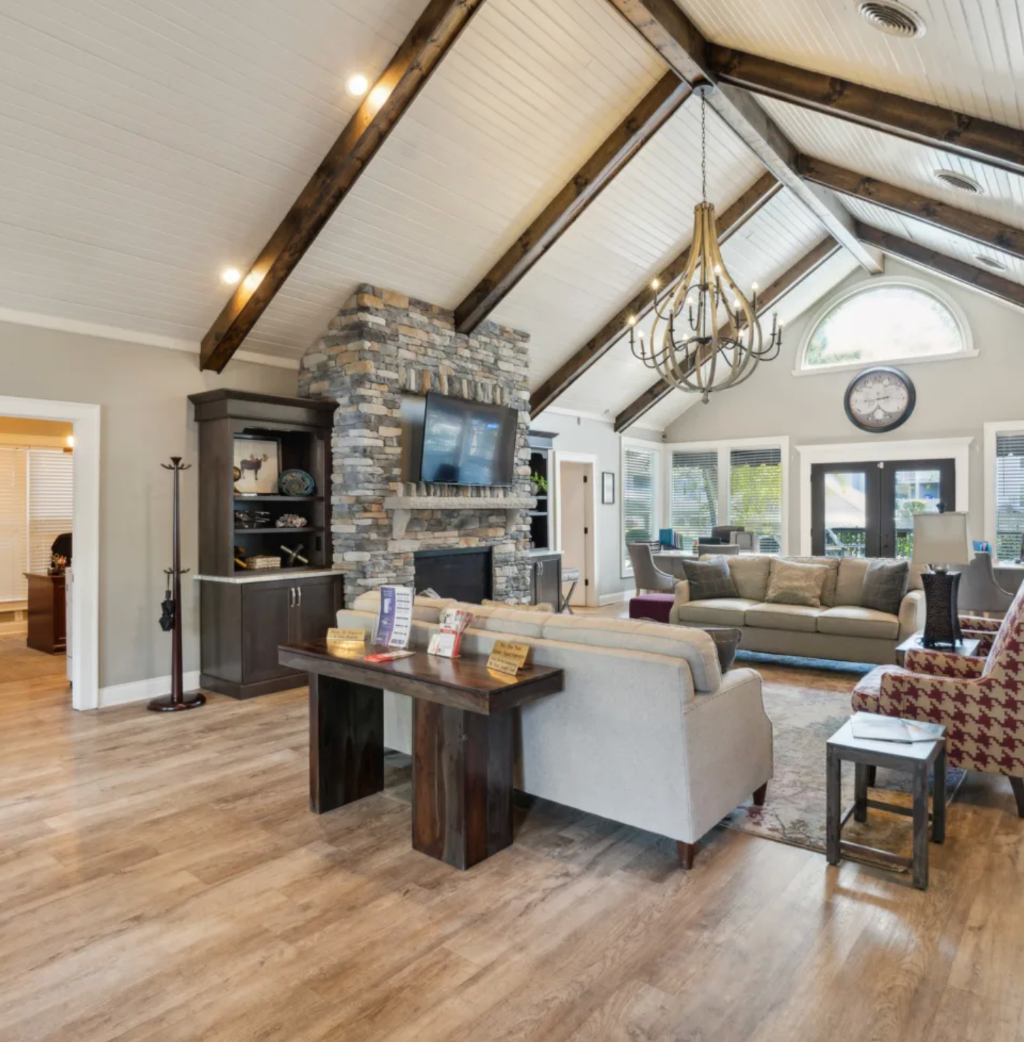 Spacious living room with stone fireplace, wood beams, chandelier, and several seating areas.