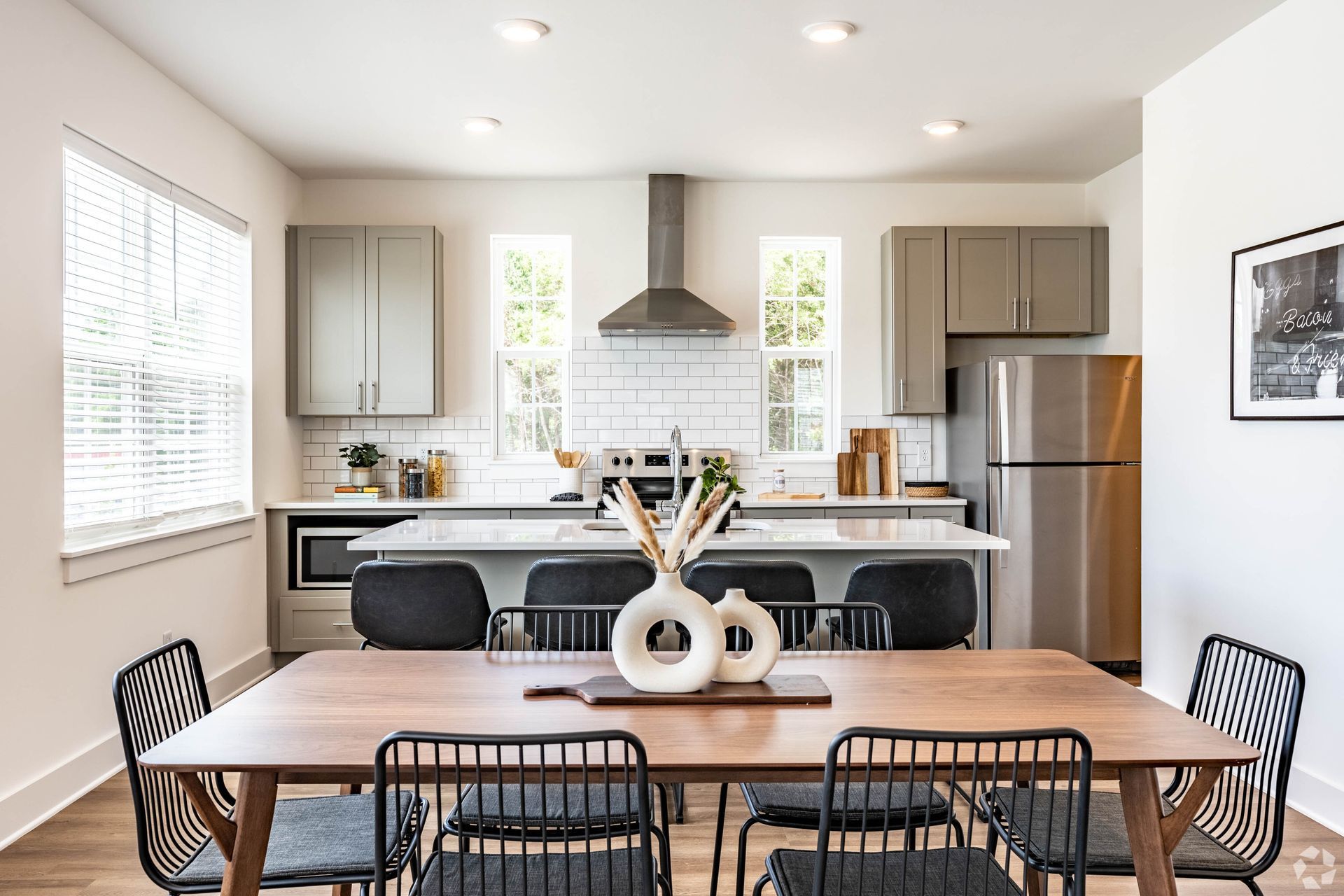 Modern kitchen and dining room with wooden table, metal chairs, and gray cabinets.