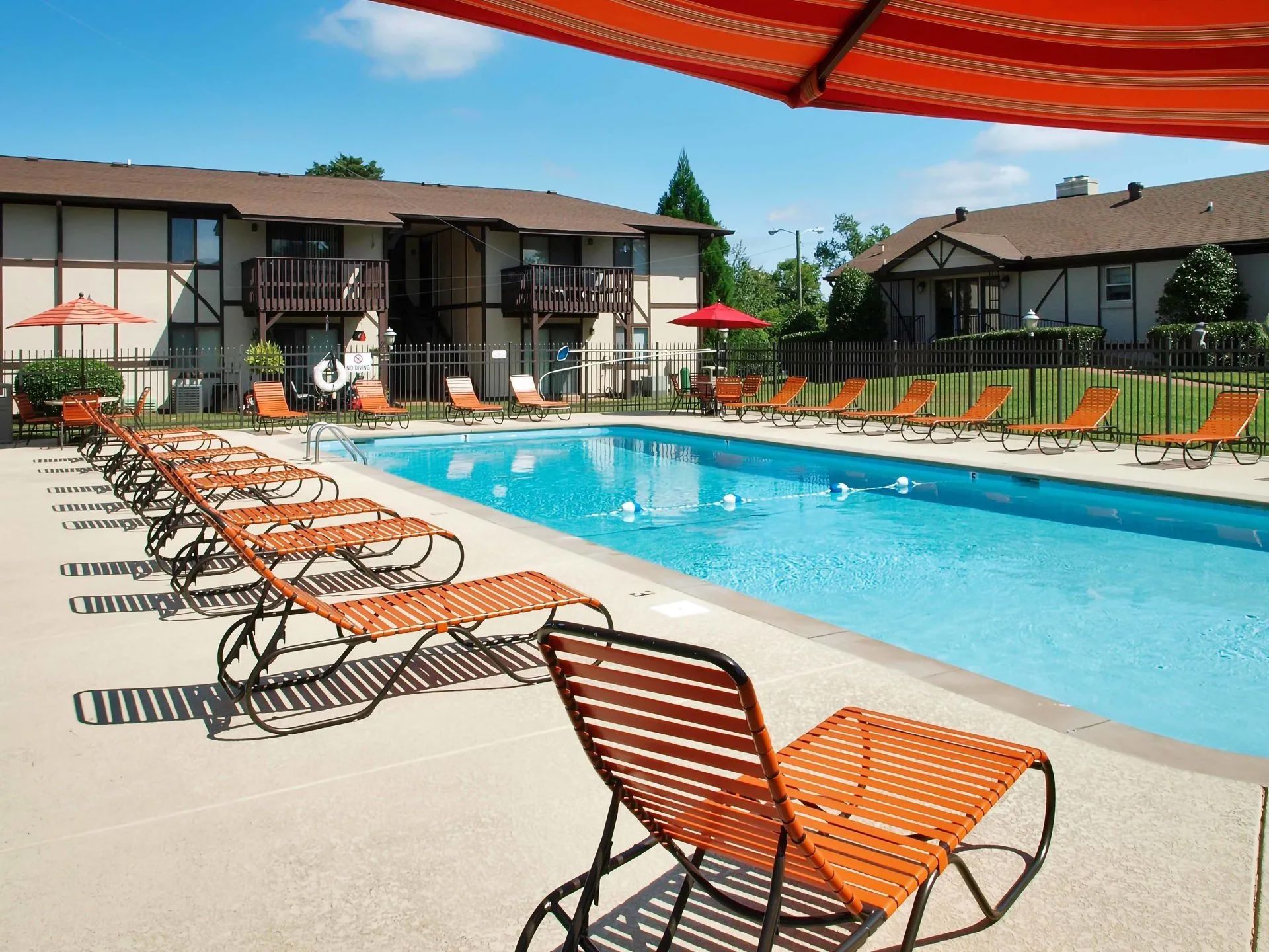 Pool area with orange lounge chairs, umbrellas, and apartment buildings in the background.