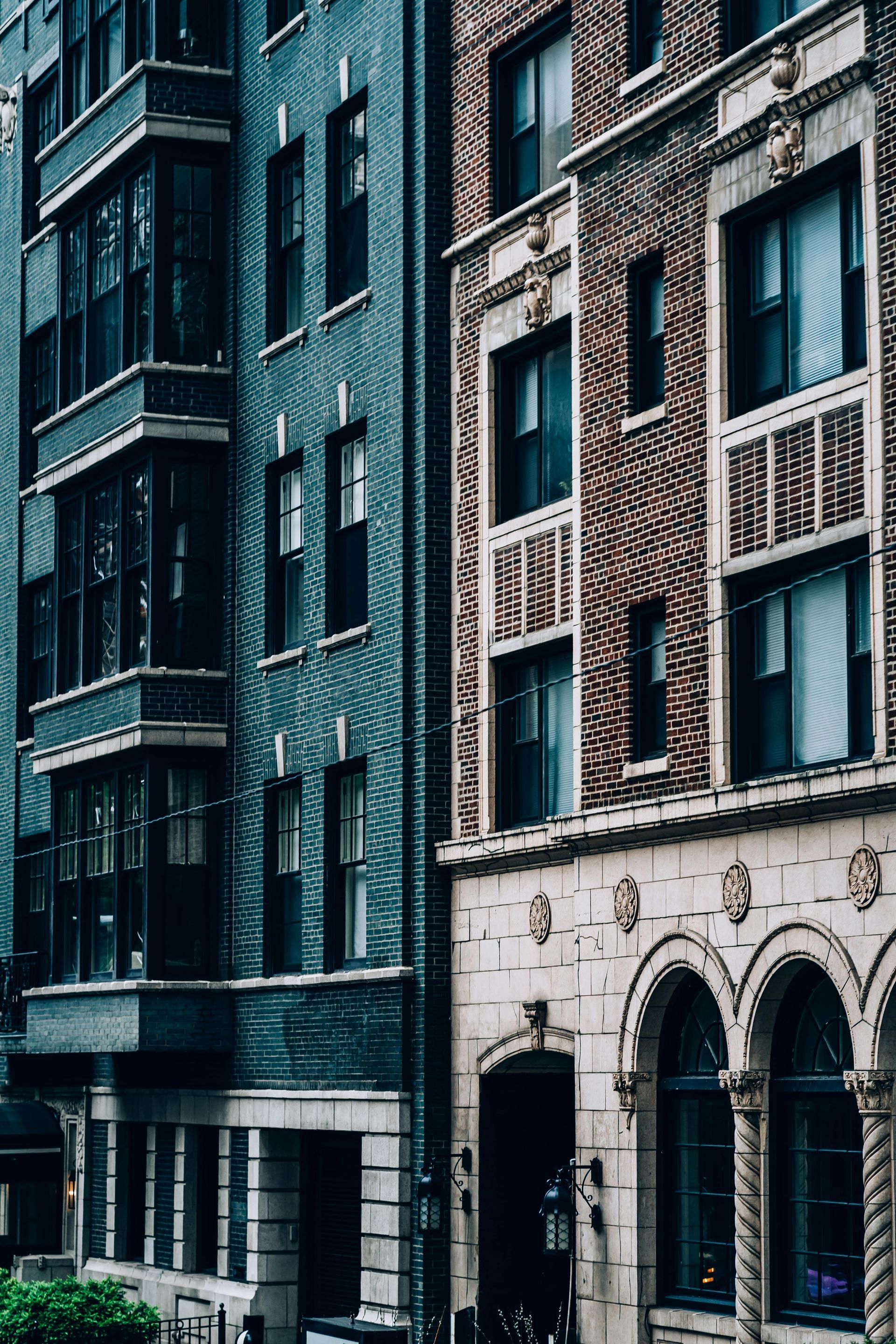 Two old buildings side by side. One is teal, the other is brick with arched windows.