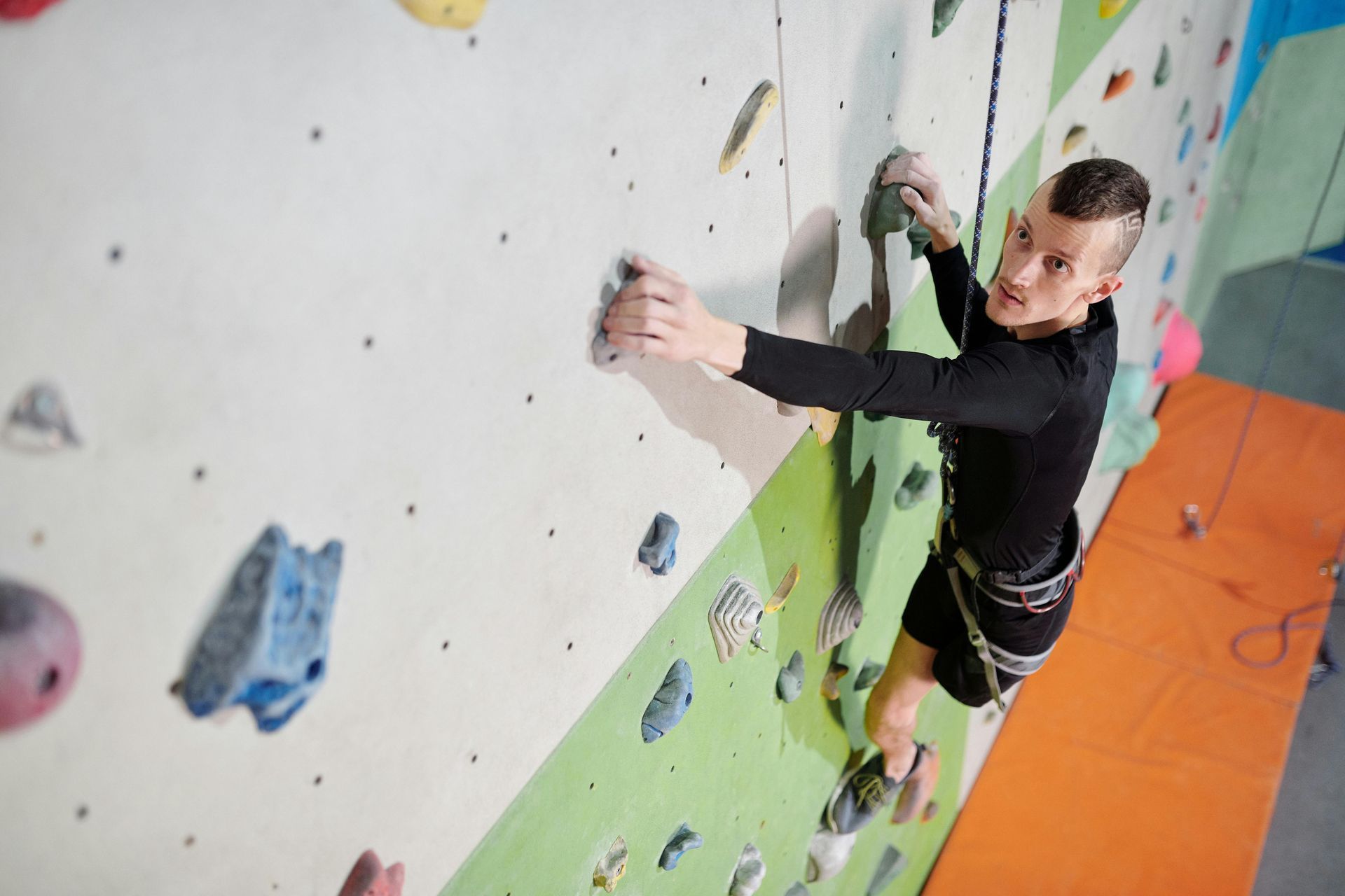 Man climbing a colorful indoor rock wall, reaching for a hold.
