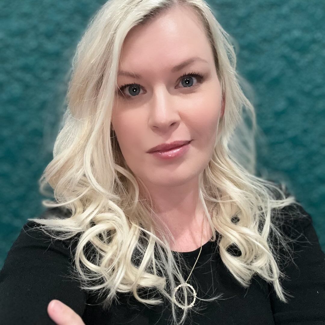 A woman with blonde hair is wearing a black shirt and a necklace.