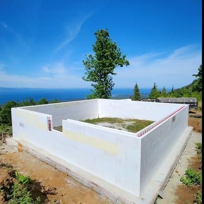 White ICF building blocks form the foundation of a structure on a grassy, ocean-view hilltop under a clear blue sky.