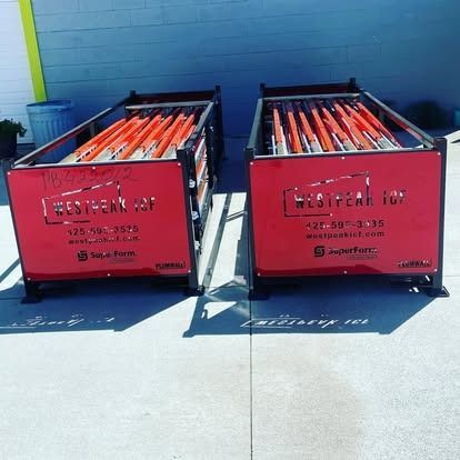 Two rectangular, red-branded storage bins filled with orange construction poles stand on a concrete surface.